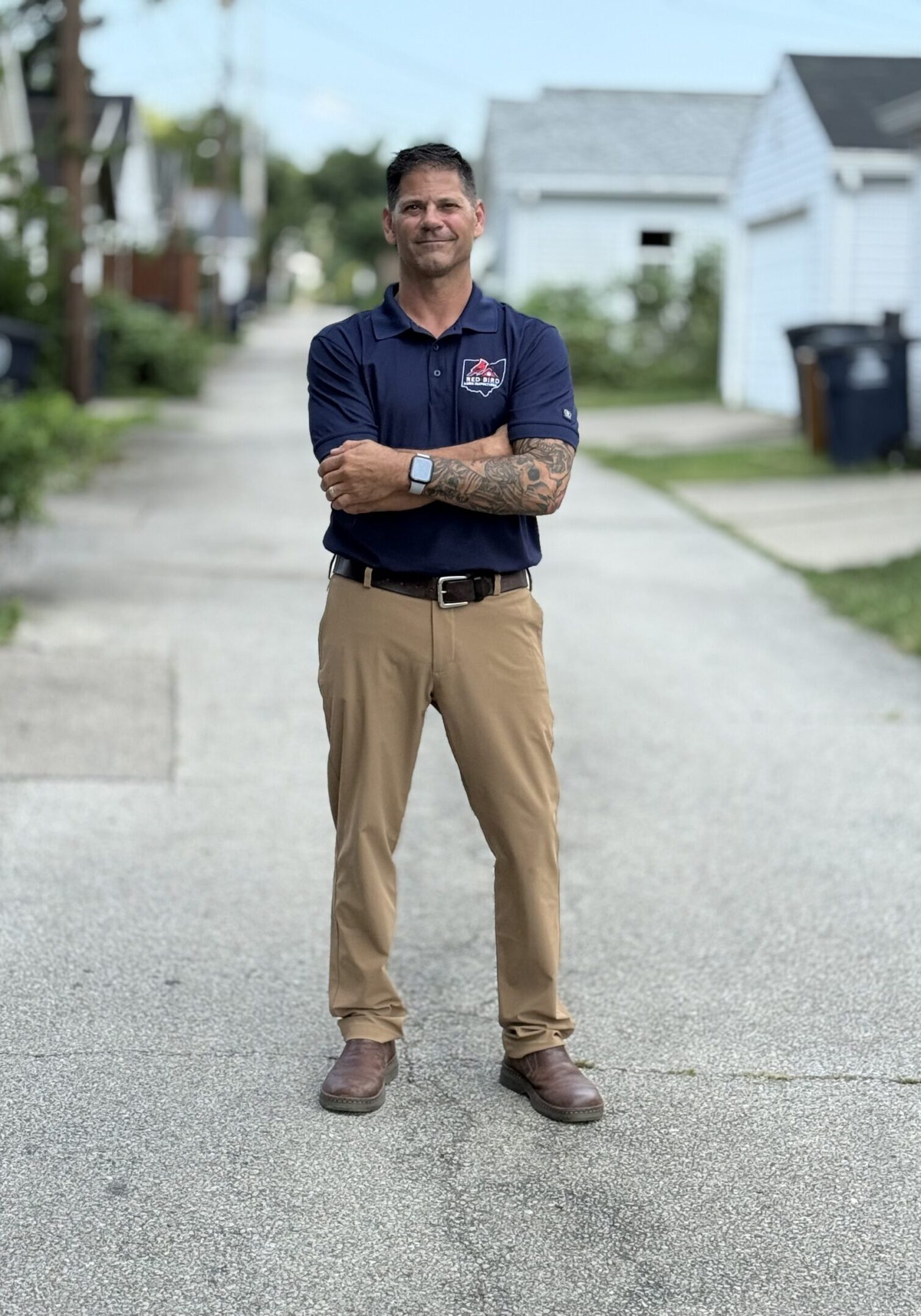 Man standing confidently with arms crossed on a suburban street.